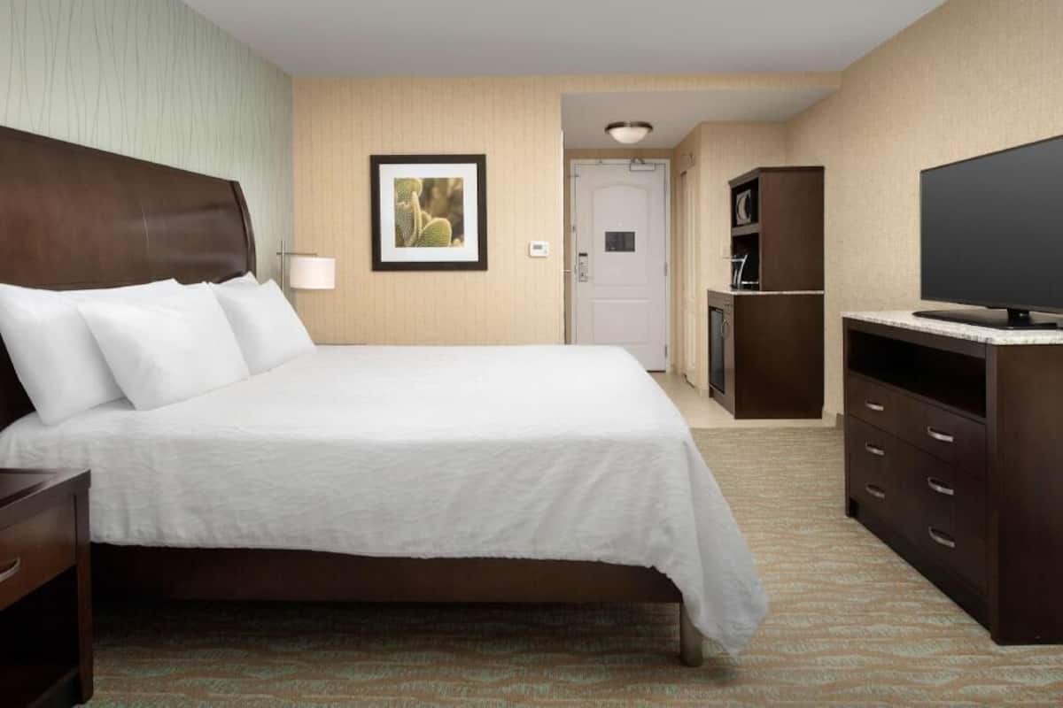 Una habitación de hotel con una cama, televisión, escritorio y puerta.