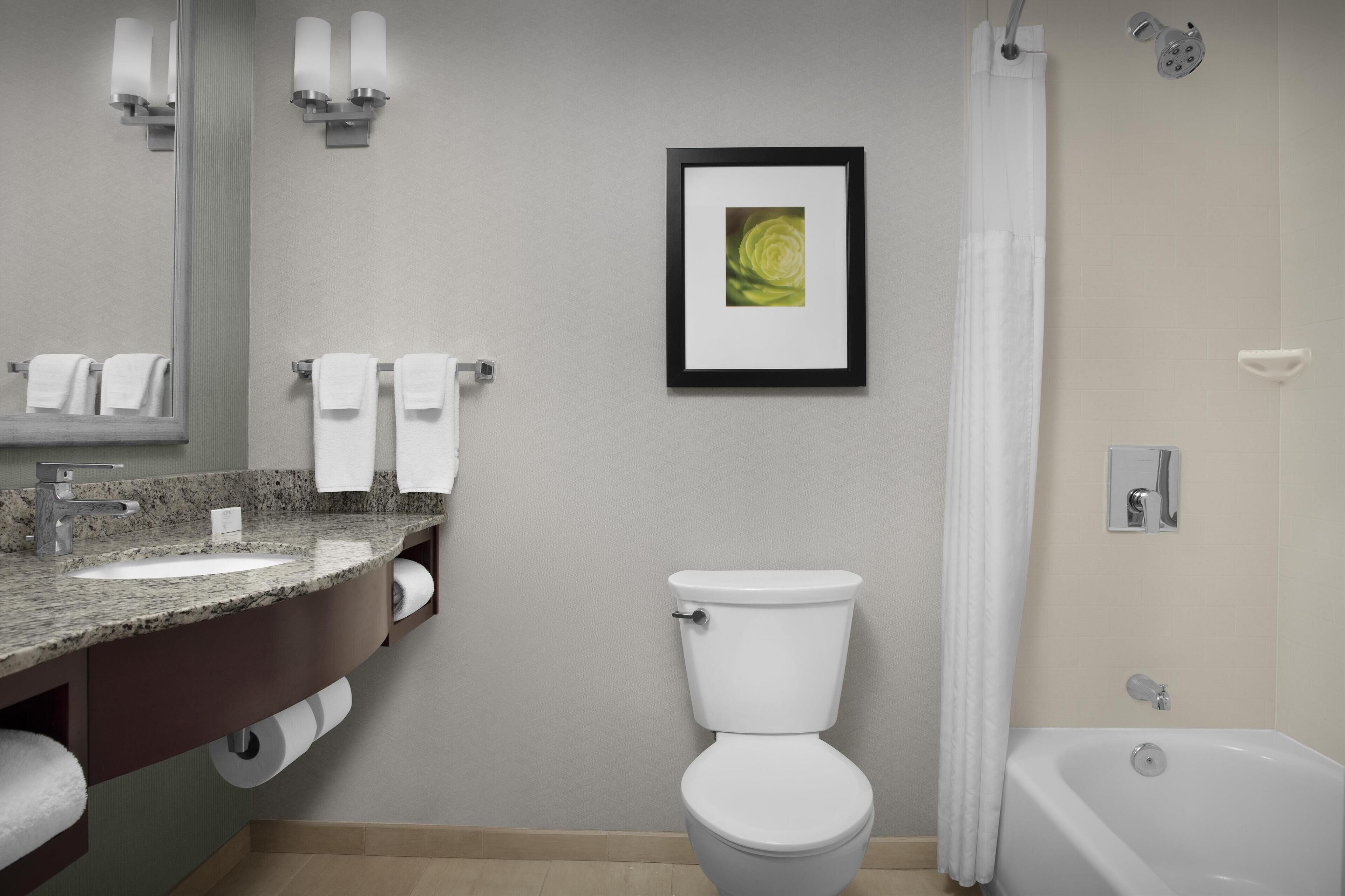 A modern bathroom with a granite countertop sink, a white toilet, and a bathtub.