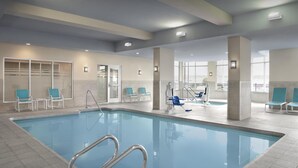 Une piscine intérieure à l’eau claire, entourée de chaises bleues et dotée d’un espace vestiaire.