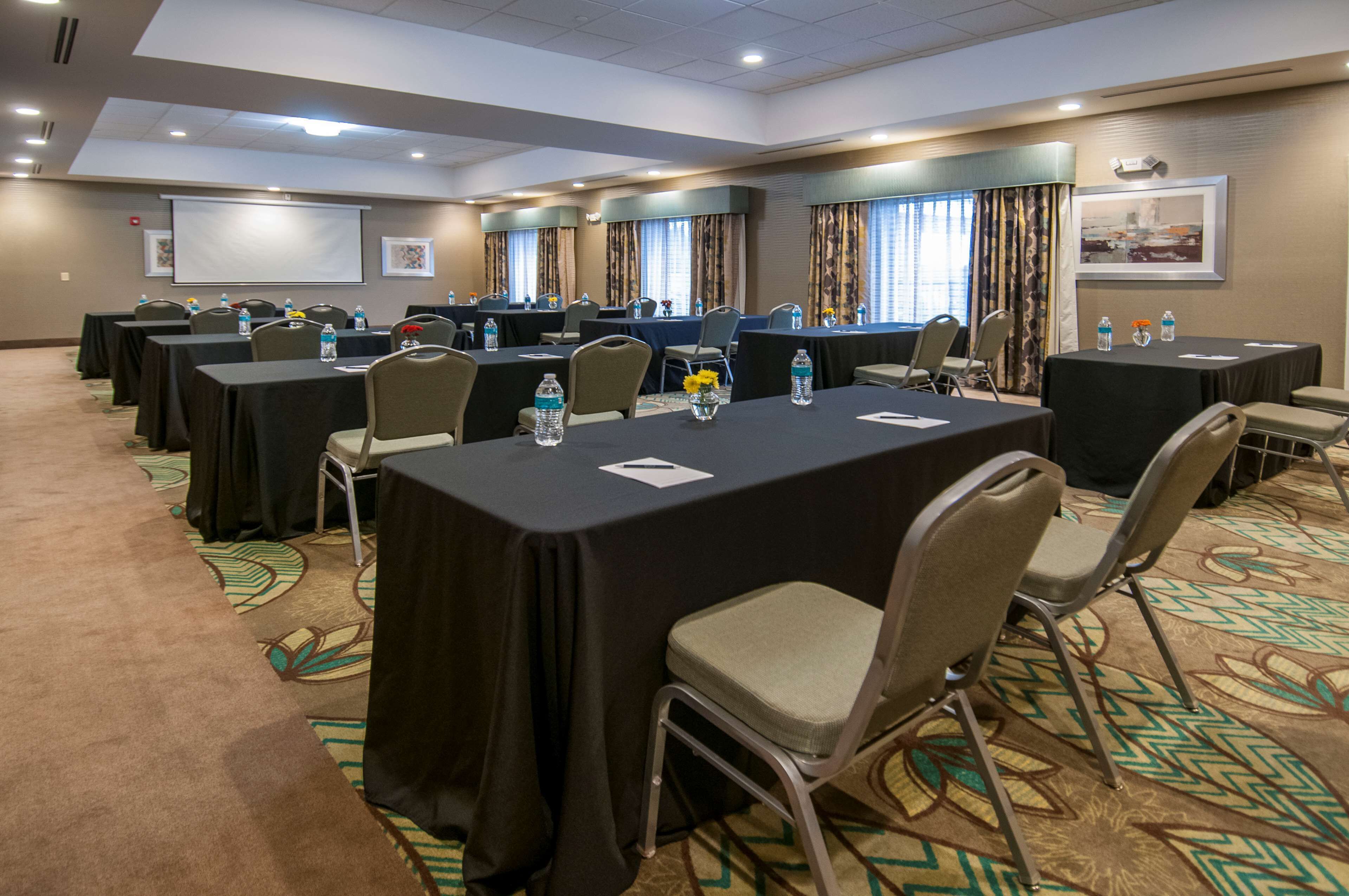 A conference room with multiple tables, chairs, and a projector screen.
