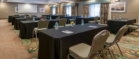 A conference room with multiple tables, chairs, and a projector screen.