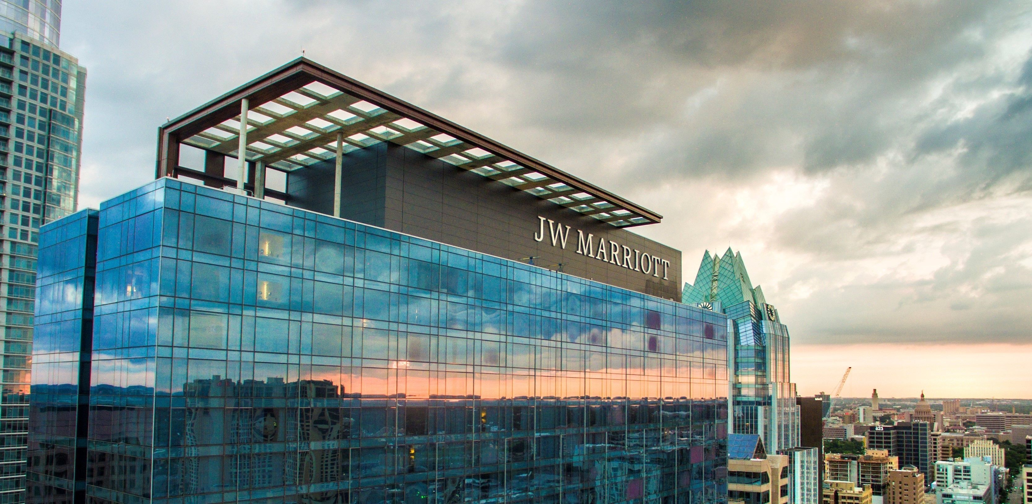 A JW Marriott hotel with a modern glass facade, large windows, and a prominent rooftop structure.
