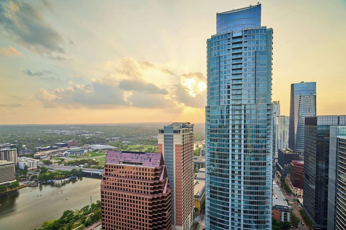 Ein Hochhaus mit einer gewölbten Glasfassade, umgeben von weiteren modernen Gebäuden und einem Fluss.
