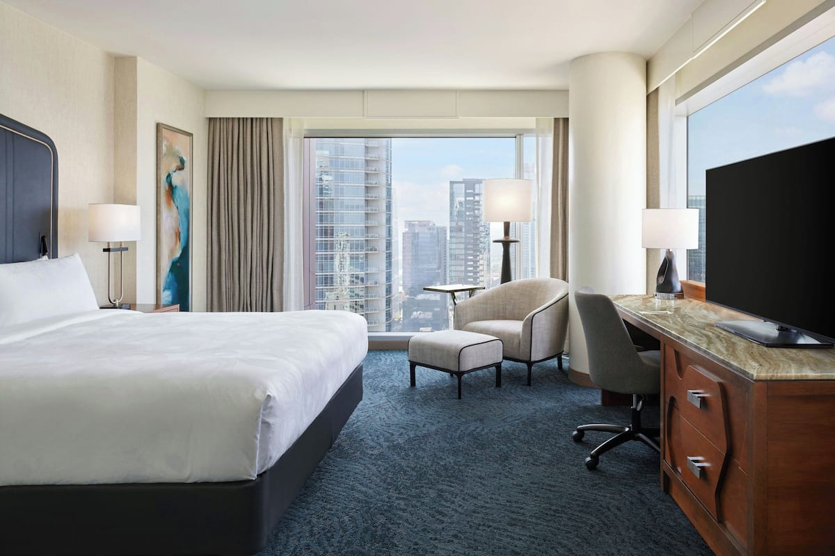Ein Hotelzimmer mit einem großen Bett, einem Schreibtisch mit Computer, einem Sessel und einem Fernseher.
