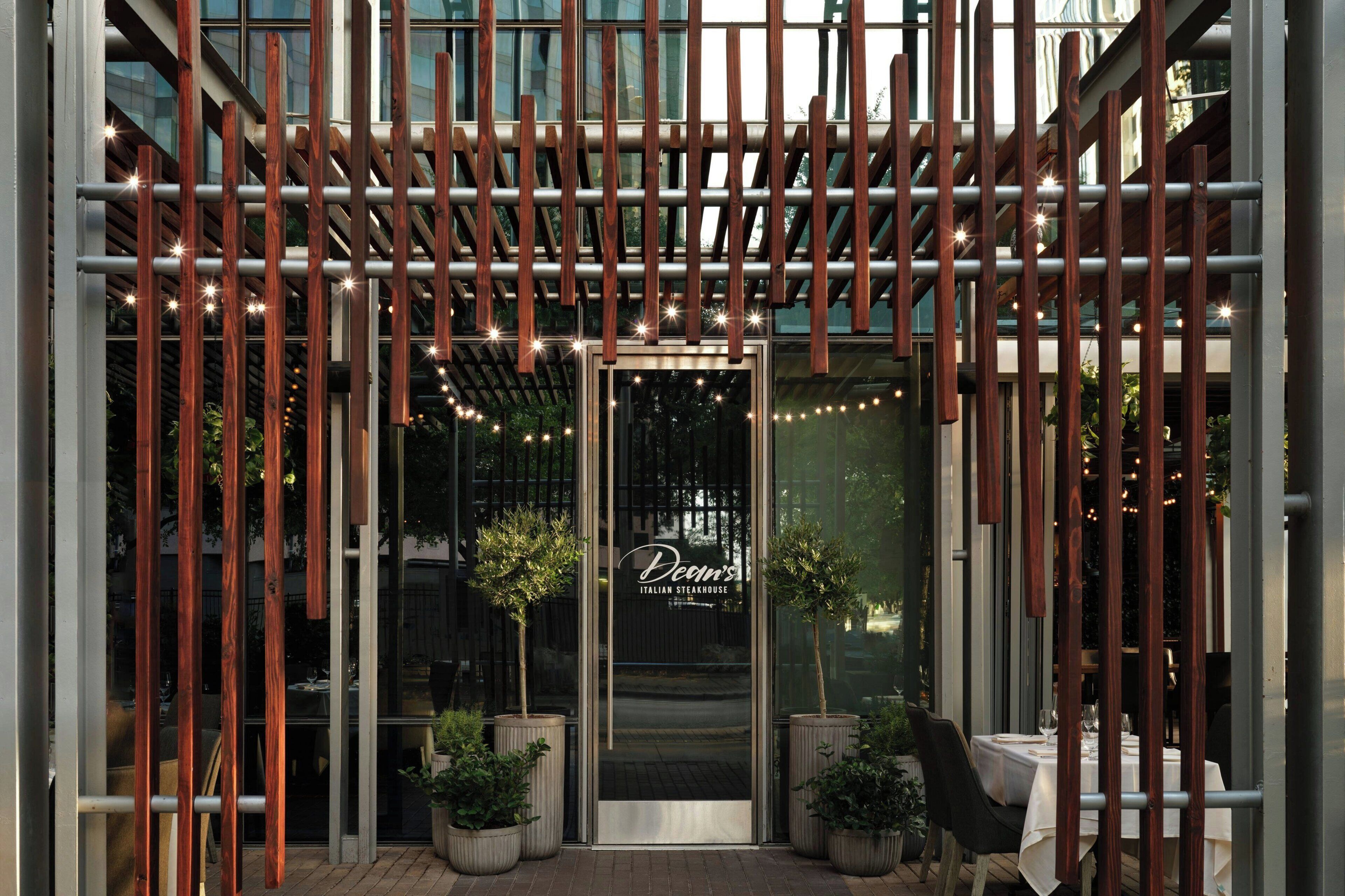 The entrance of Decov's Italian Steakhouse with a modern wooden pergola and potted plants.