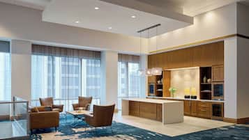 A modern hotel lobby with a seating area, a kitchen, and large windows.