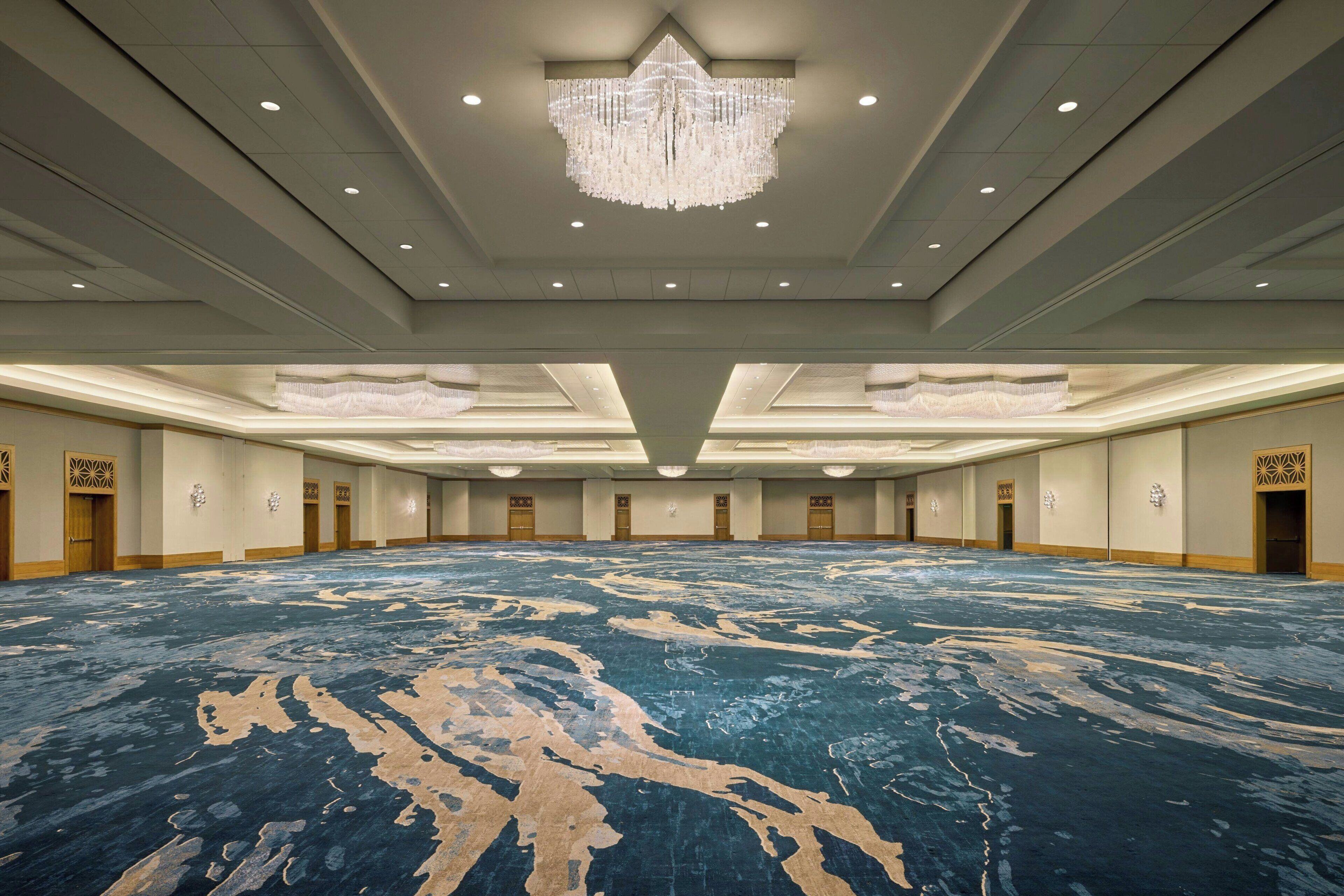 A large conference room with a patterned carpet, a chandelier, and symmetrical doorways.