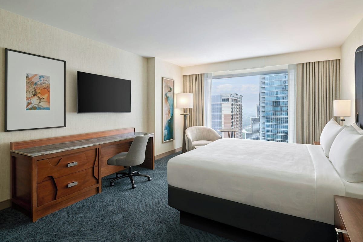 Ein Hotelzimmer mit einem großen Bett, einem Schreibtisch mit Stuhl, einem Flachbildfernseher und einem Fenster mit Blick auf die Stadt.