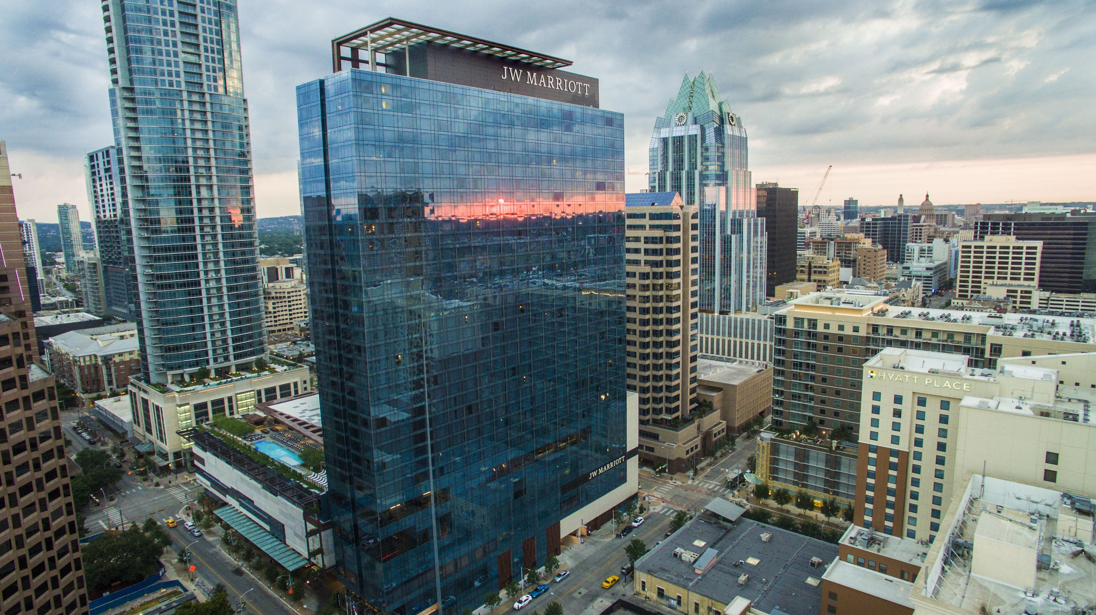 A JW Marriott hotel with a modern glass facade, surrounded by other high-rise buildings in a cityscape.