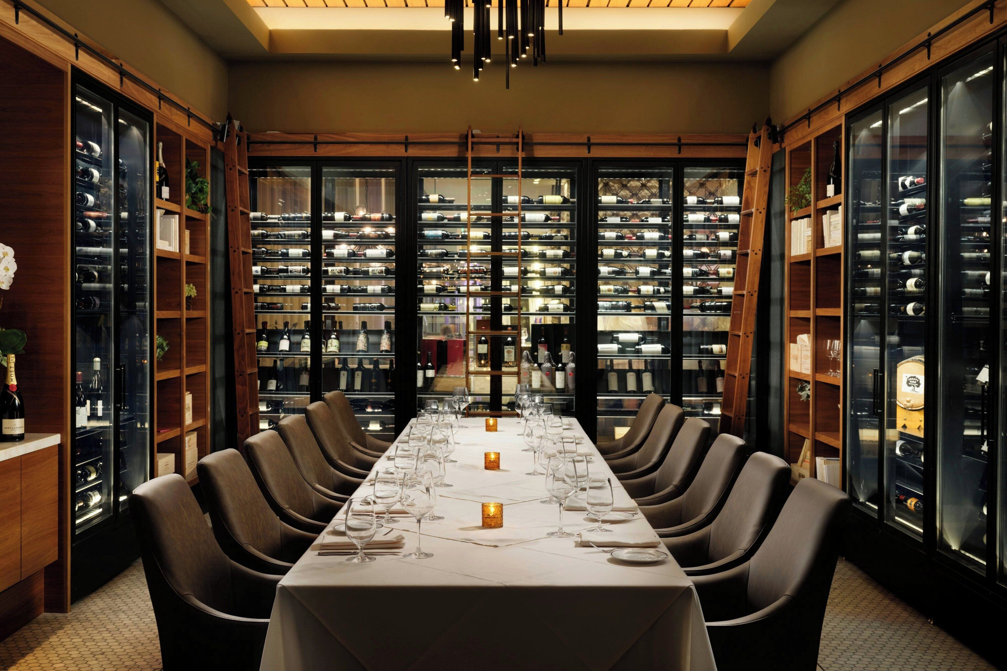 Una larga mesa de comedor con sillas, rodeada de estanterías para vinos y repisas.