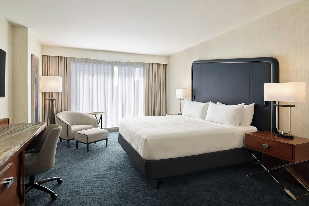 Ein Hotelzimmer mit einem großen Bett, einem Schreibtisch, einem Sessel und einem Nachttisch mit Lampen.