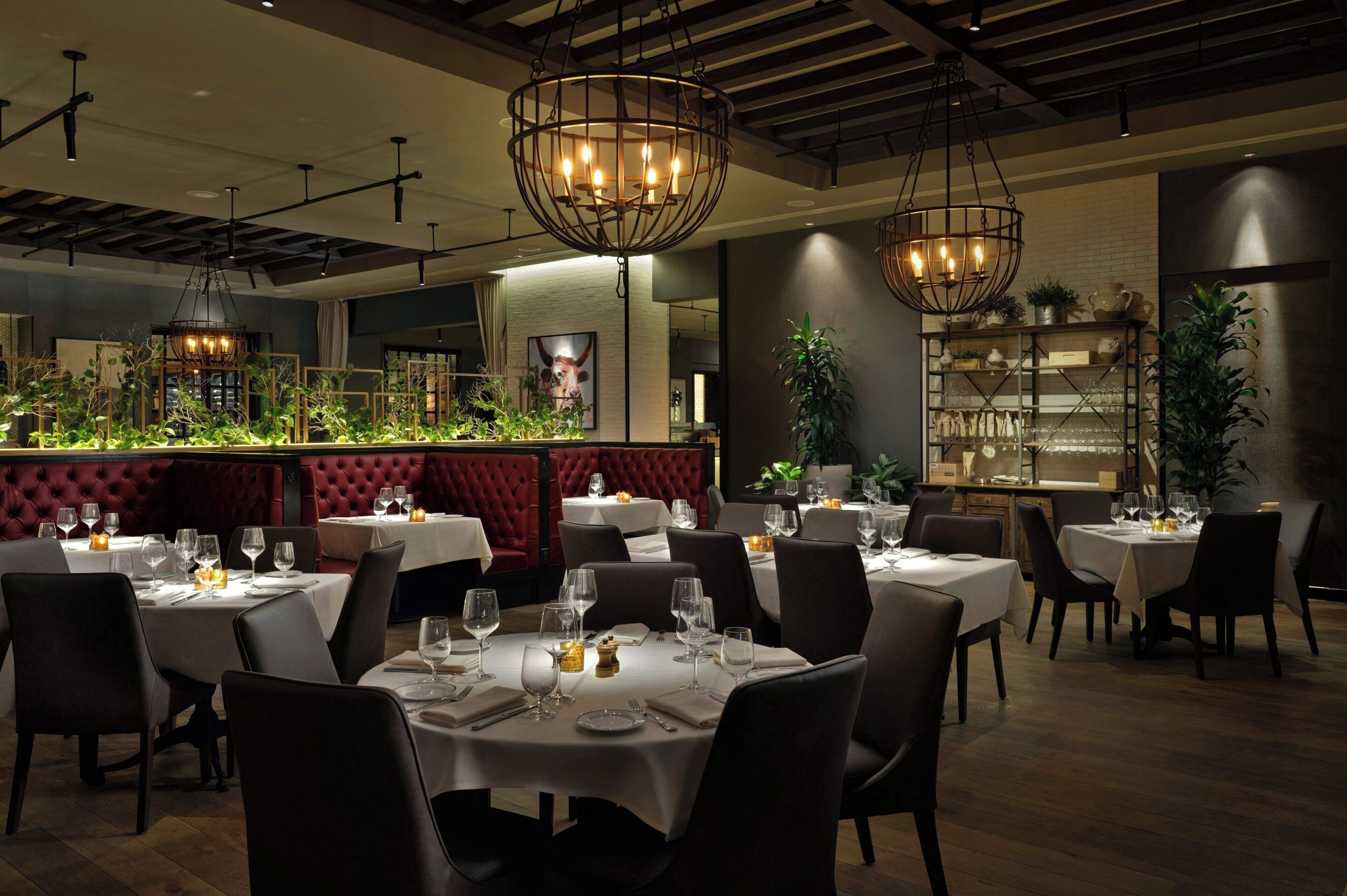 Un restaurant avec des tables rondes, des chaises sombres et des lustres suspendus.