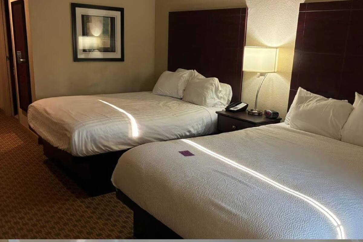 Ein Hotelzimmer mit zwei Betten, einem Nachttisch mit Lampe und einem gerahmten Bild an der Wand.