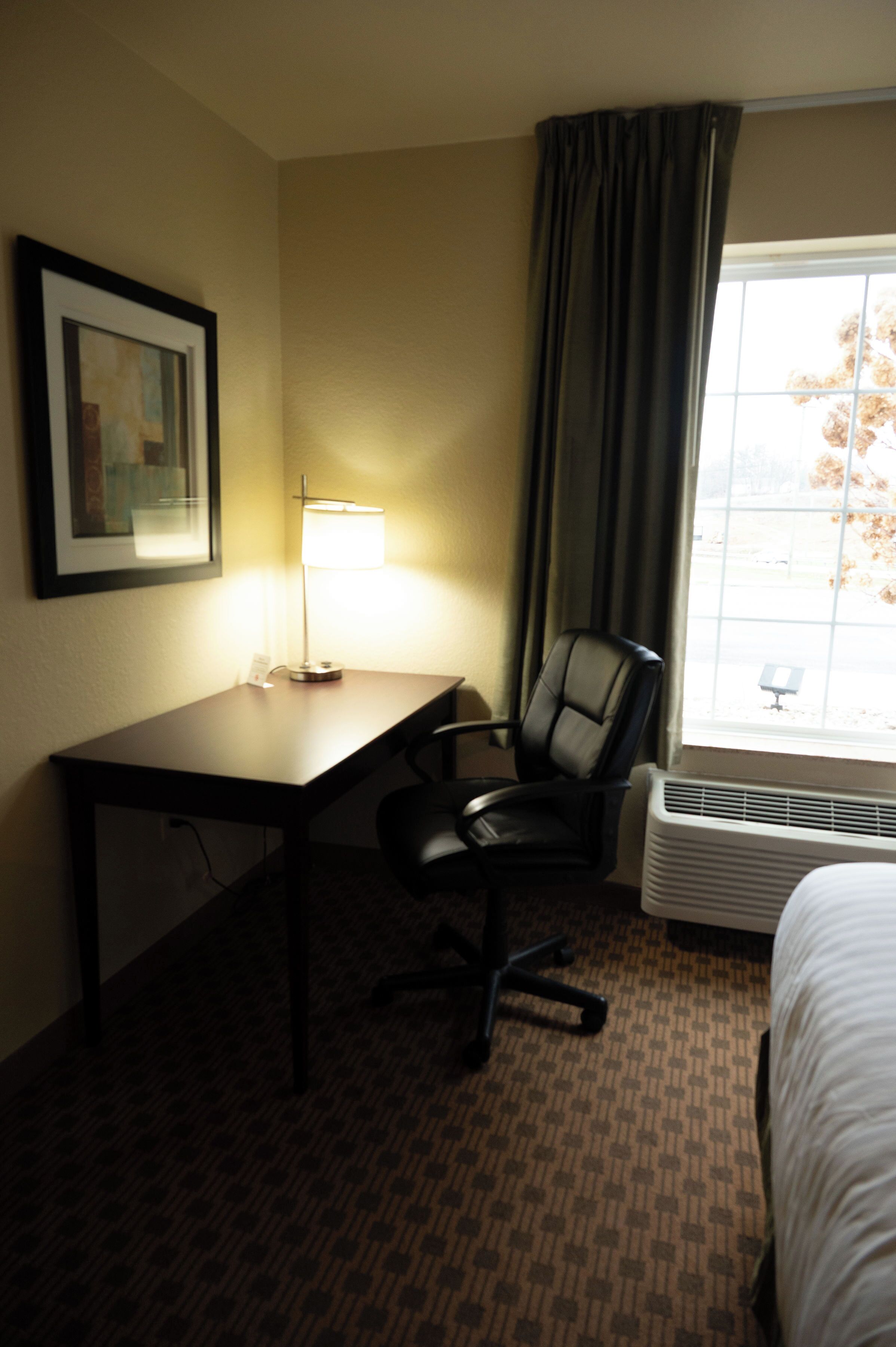 Una habitación de hotel con escritorio, silla, cama y ventana con cortinas.