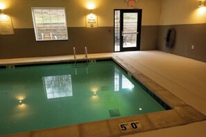 Una piscina interior con un cartel que dice 'No se Permite el Clavado', una ventana con vistas y una puerta que da al exterior.