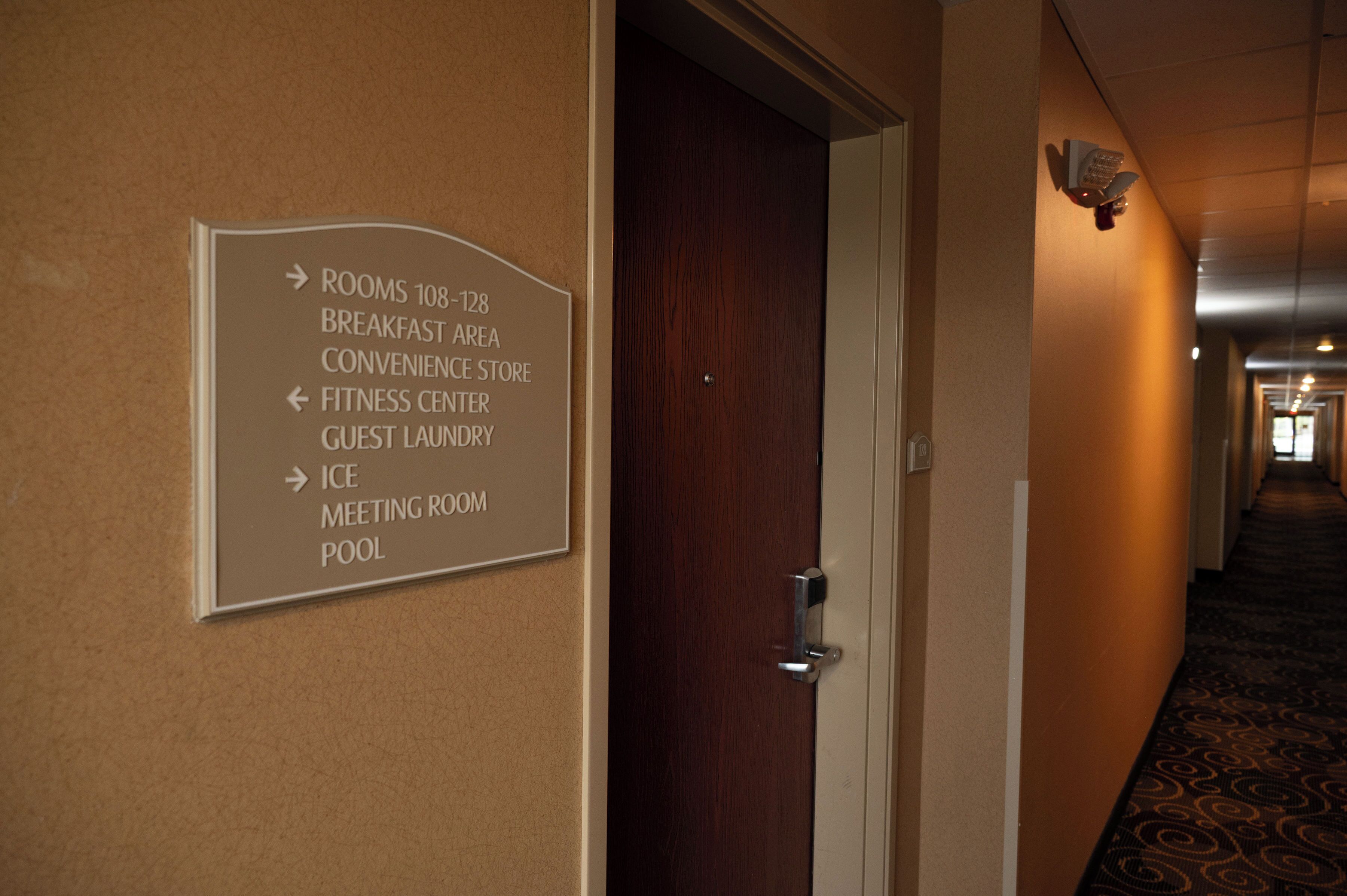 A hotel hallway with a directional sign indicating amenities such as rooms, breakfast area, fitness center, guest laundry, ice, meeting room, and pool.