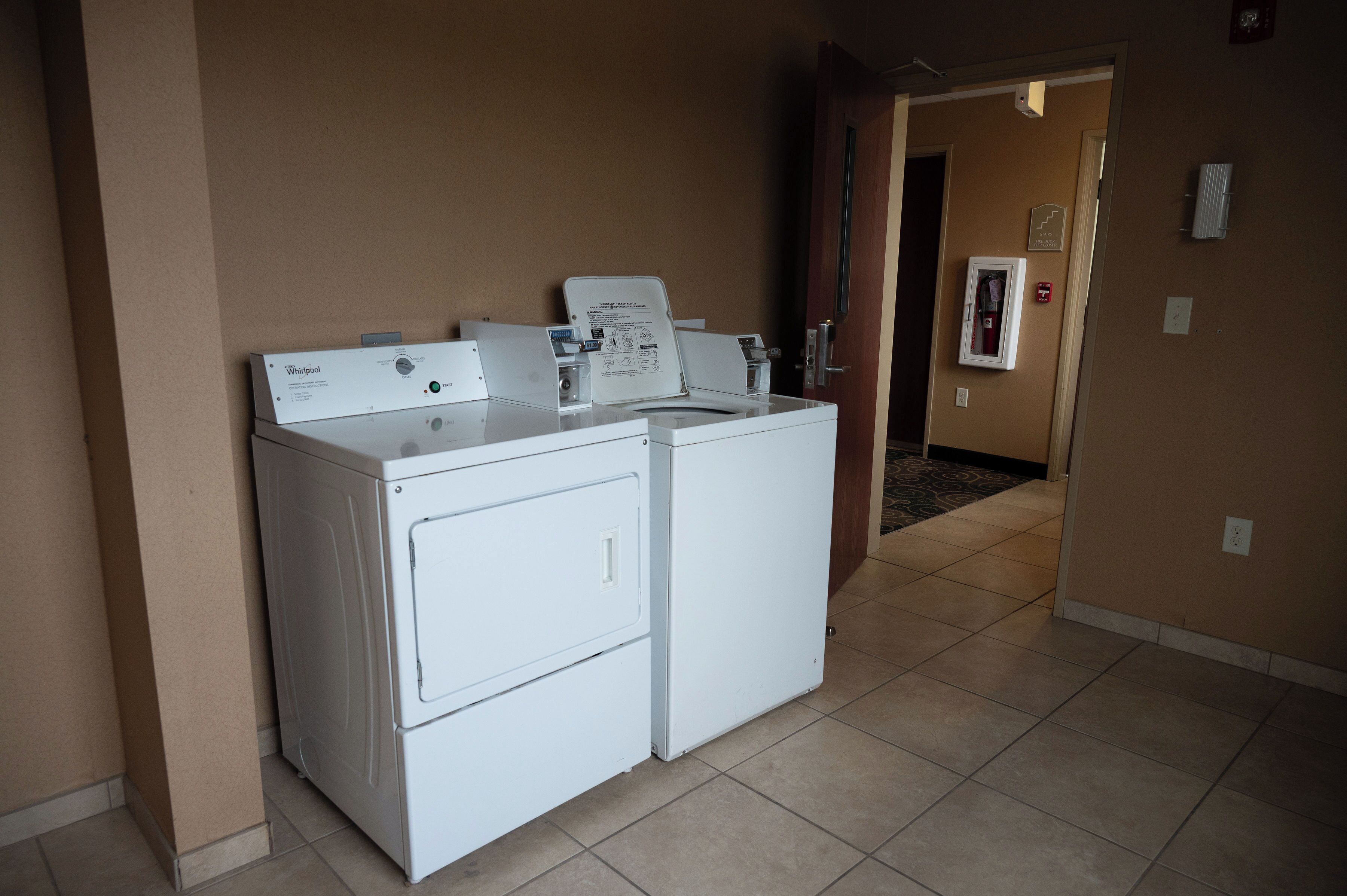 A laundry area with two white washers and dryers, a control panel, and a door leading to another room.