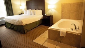 A hotel room with a large bed, a bedside table with a lamp, a small nightstand, and a separate bathroom with a bathtub.