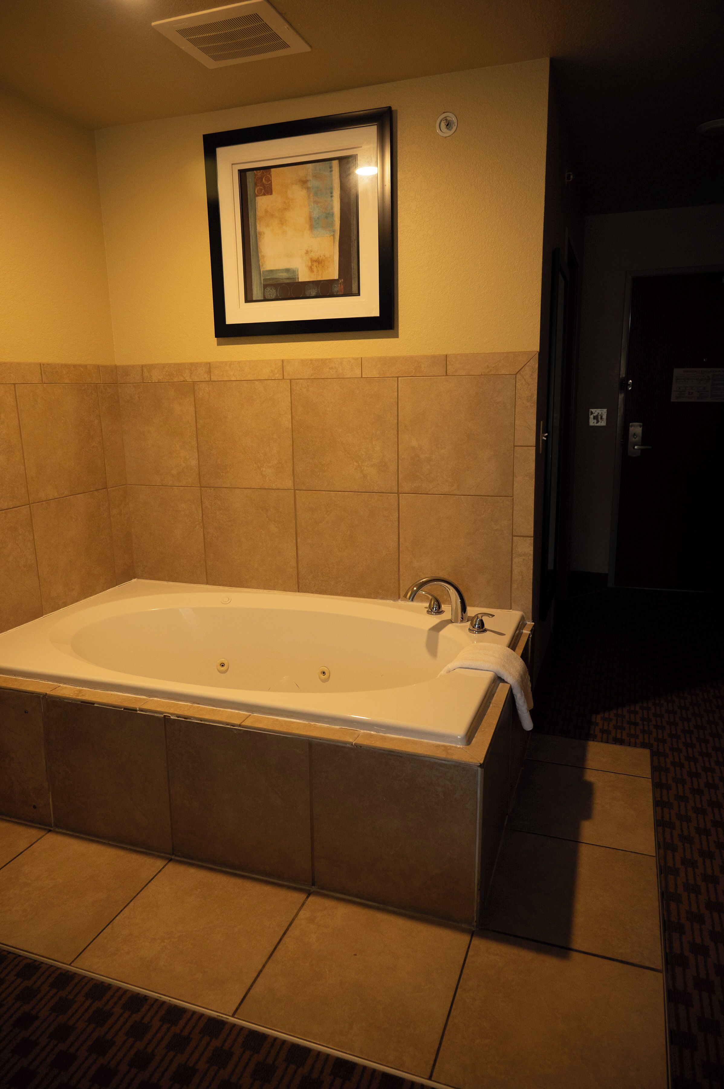 Eine große Badewanne in einem Hotelbad mit einem gerahmten Bild darüber.
