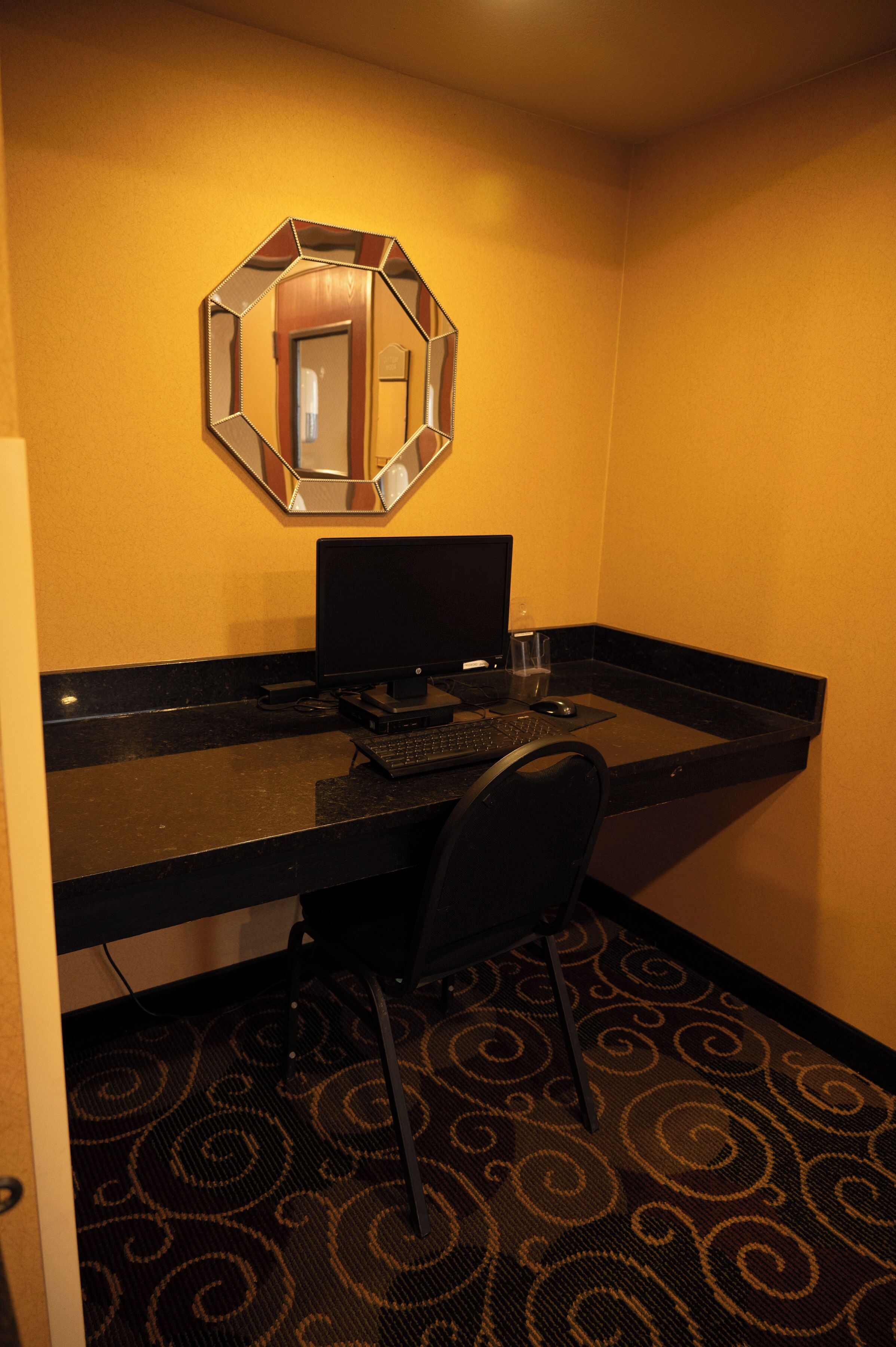 Ein Hotelzimmer mit Schreibtisch, Computer, Stuhl, Spiegel und einem gemusterten Teppich.