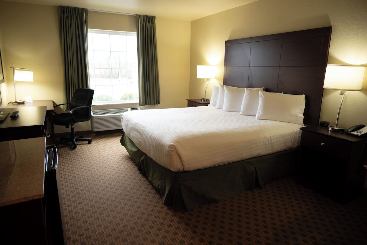 Ein Hotelzimmer mit Bett, Schreibtisch, Stuhl, Lampen und einem Fenster mit Vorhängen.