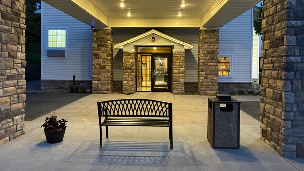A covered entrance with a bench and a trash can, flanked by stone pillars and a building entrance.
