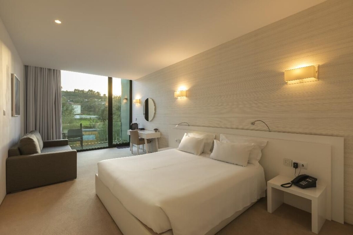 A hotel room with a large bed, a desk, a chair, a small table, and a phone on a nightstand.