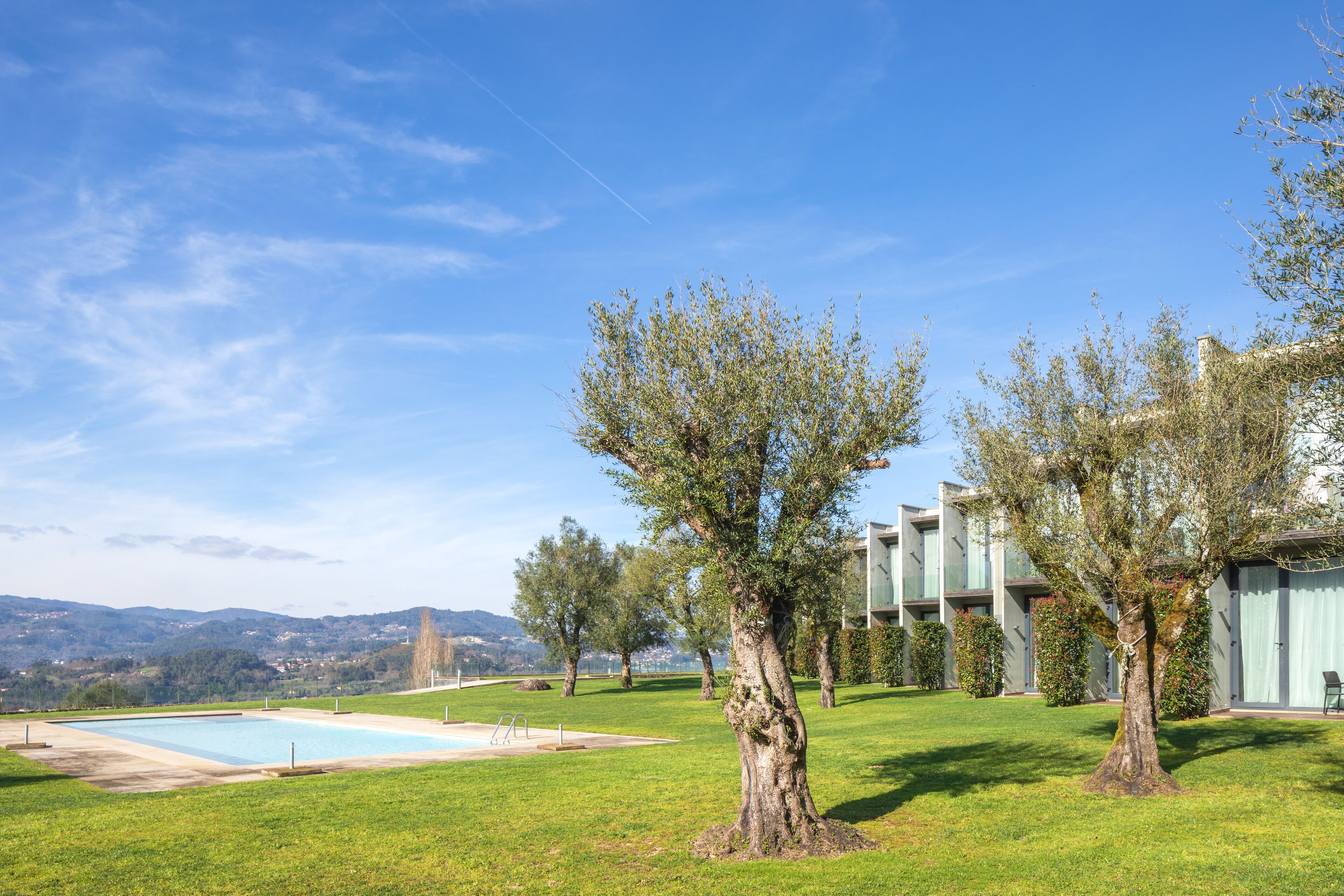 Zona de piscina con una vista despejada del paisaje circundante, incluyendo colinas y un edificio con grandes ventanales.
