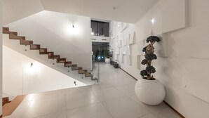 Un interior moderno con una escalera, un gran jarro blanco con un bonsái y una pared decorada con arte abstracto.
