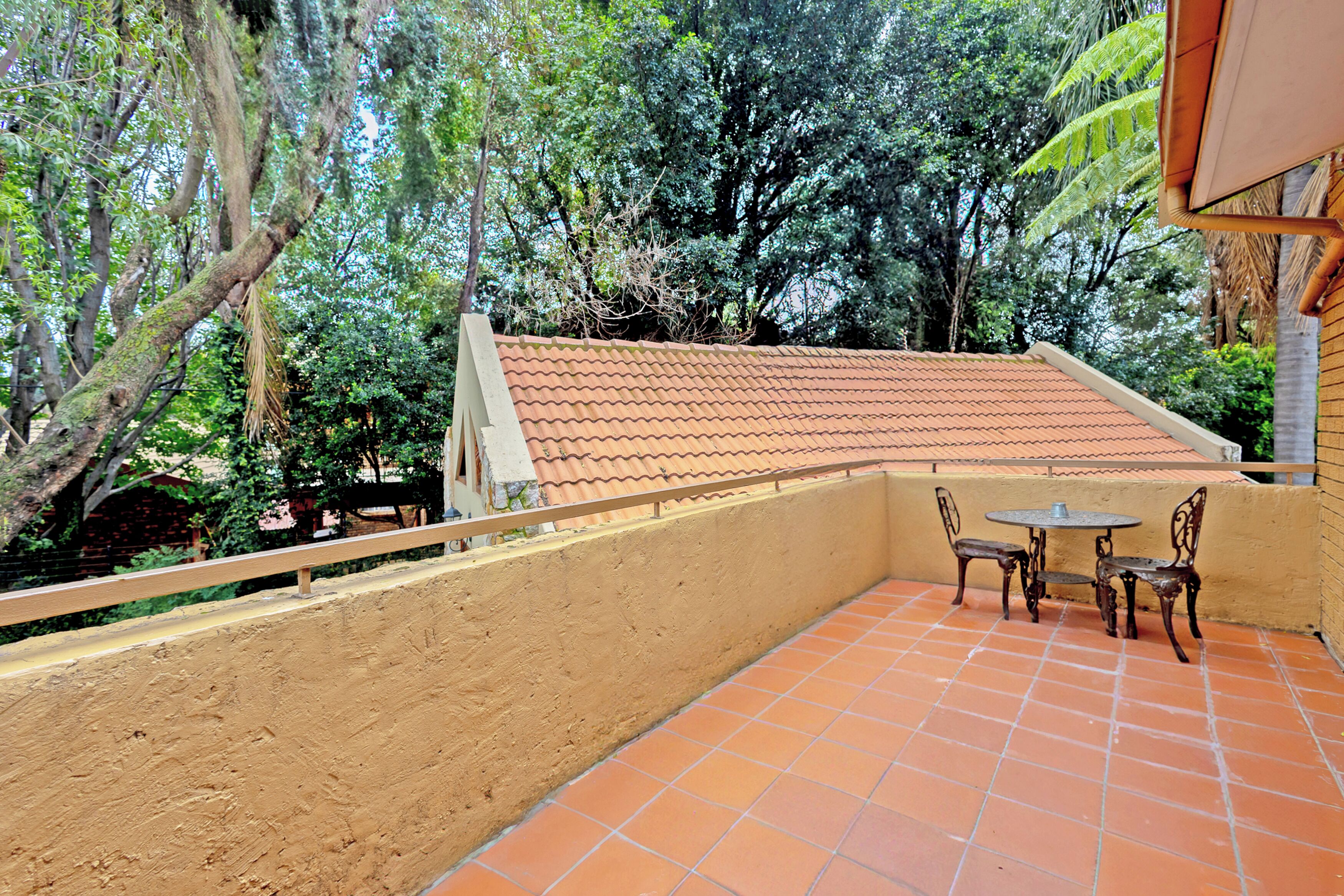 A balcony with a tiled floor, a table with two chairs, and a view of surrounding trees.