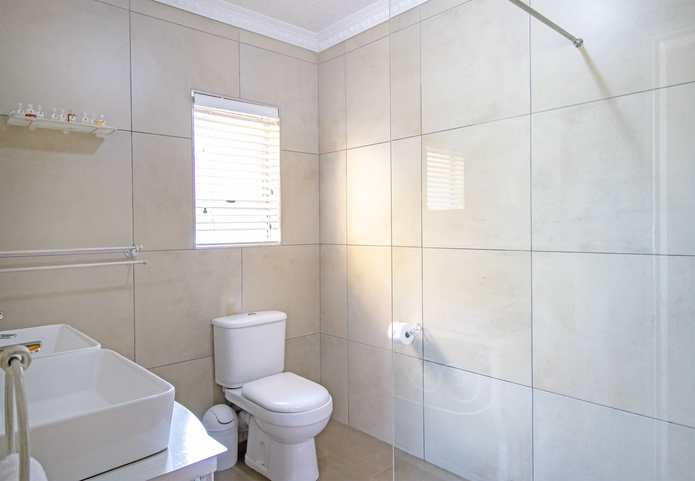 Une salle de bain équipée de toilettes, d’un lavabo et d’une fenêtre avec des stores.