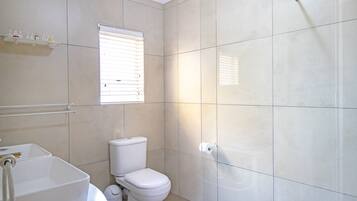 Un baño con inodoro, lavamanos y ventana con persianas.