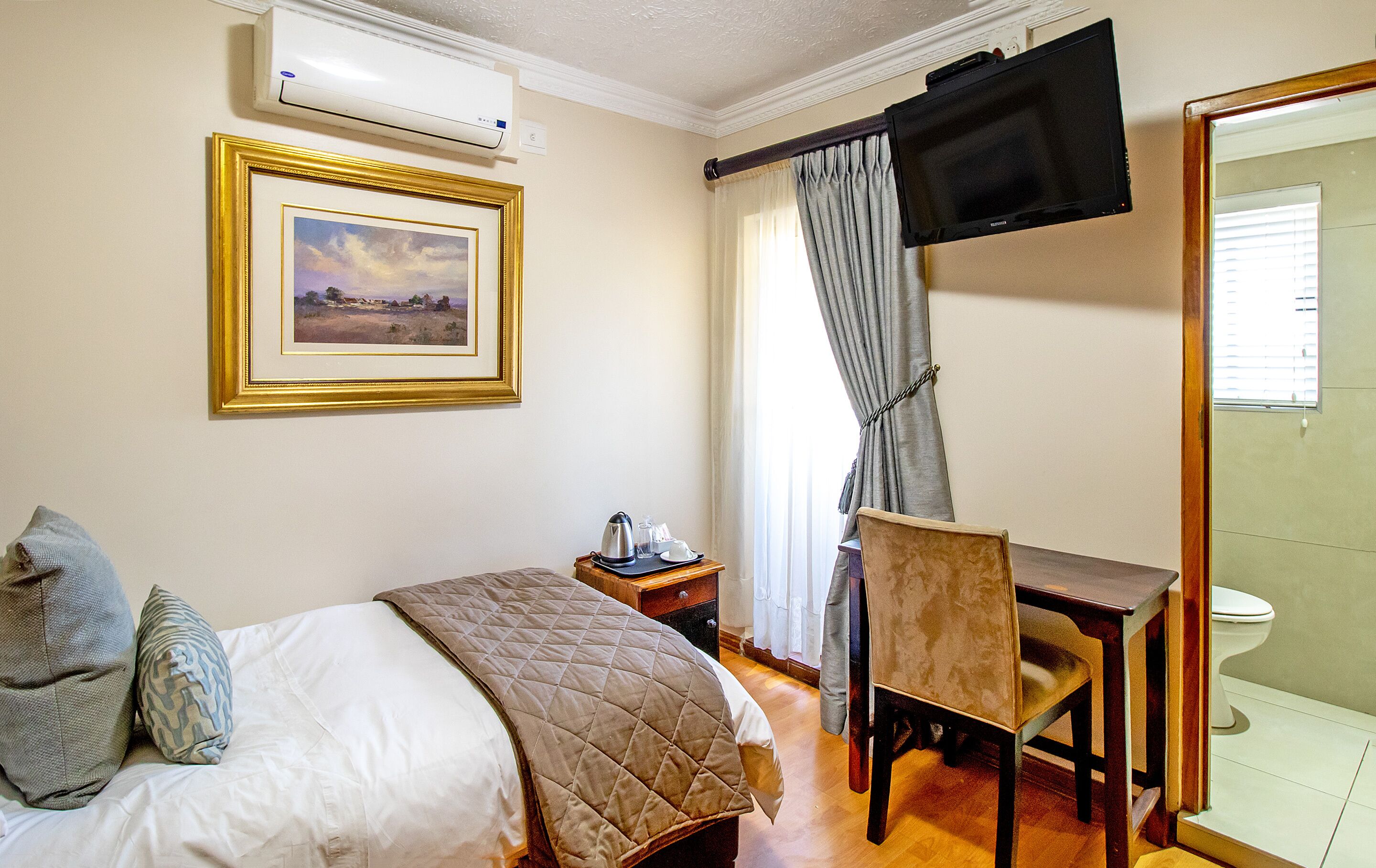 A hotel room with a bed, a desk, a chair, a television, and a framed picture on the wall.