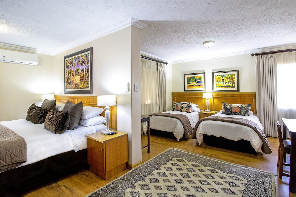 A hotel room with two beds, a wooden headboard, a nightstand, a lamp, a rug, and two framed pictures on the wall.