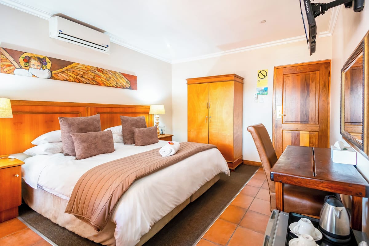 A hotel room with a bed, bedside table, lamp, wardrobe, and a desk with a mirror.