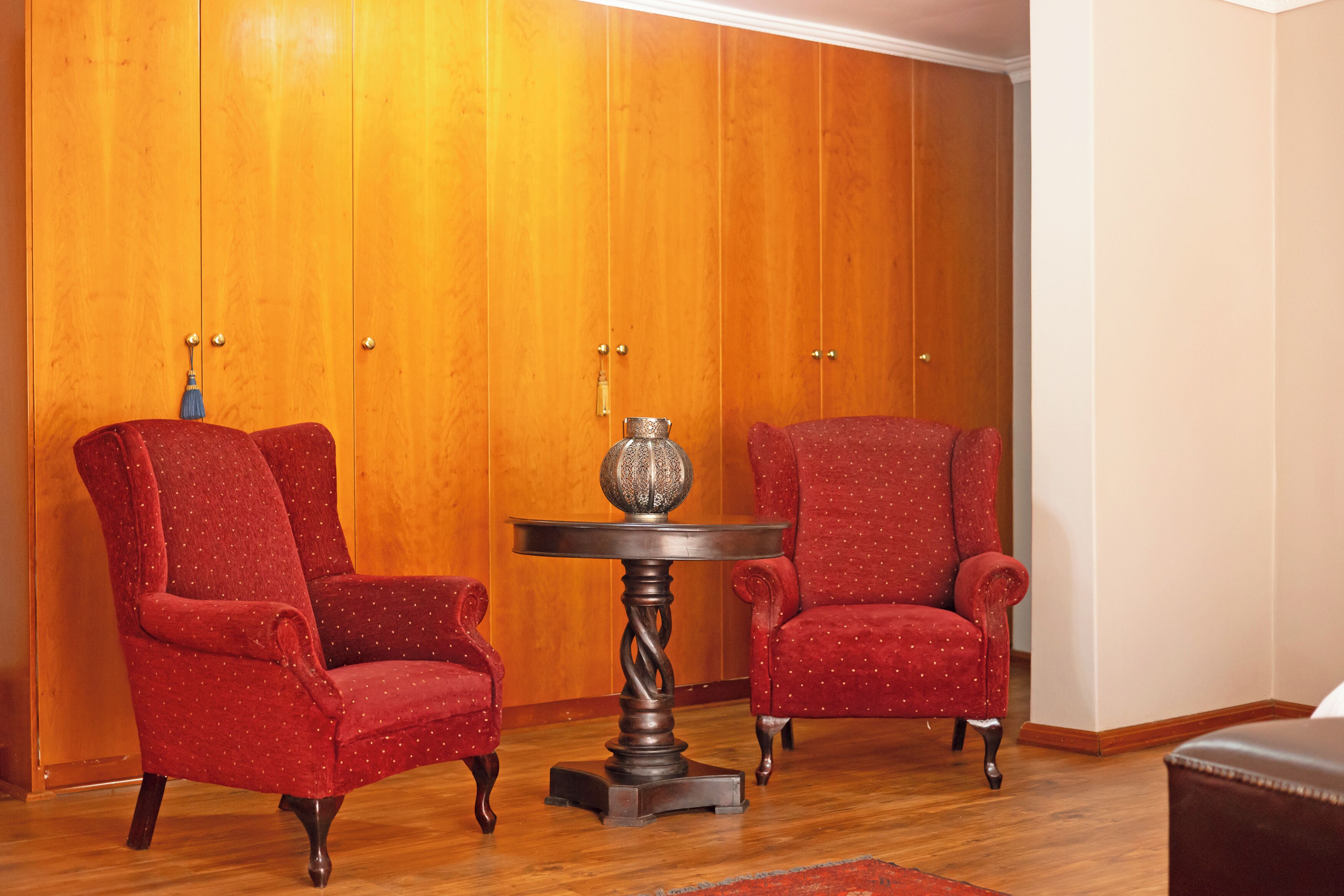Una habitación con dos sillones tapizados en rojo, suelo de madera y un armario de madera con dos puertas.