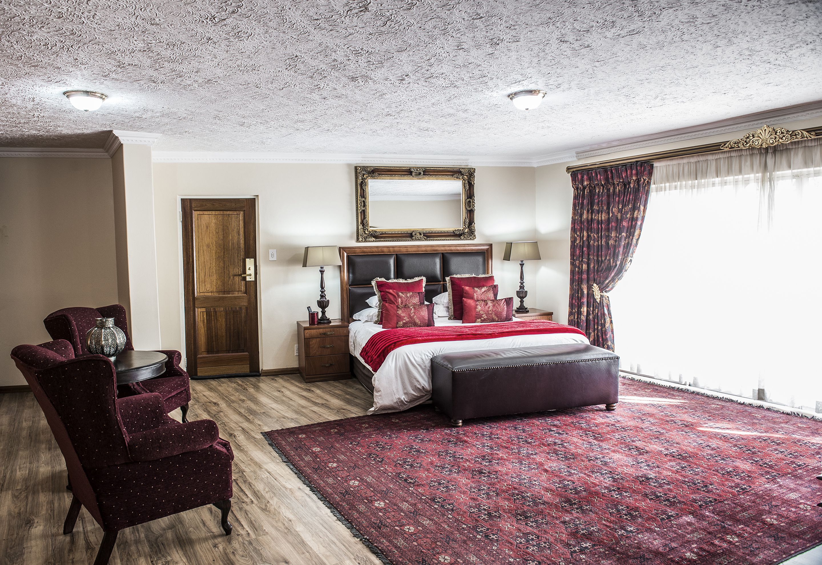 A bedroom with a large bed, a wooden door, a round table, and a chair.