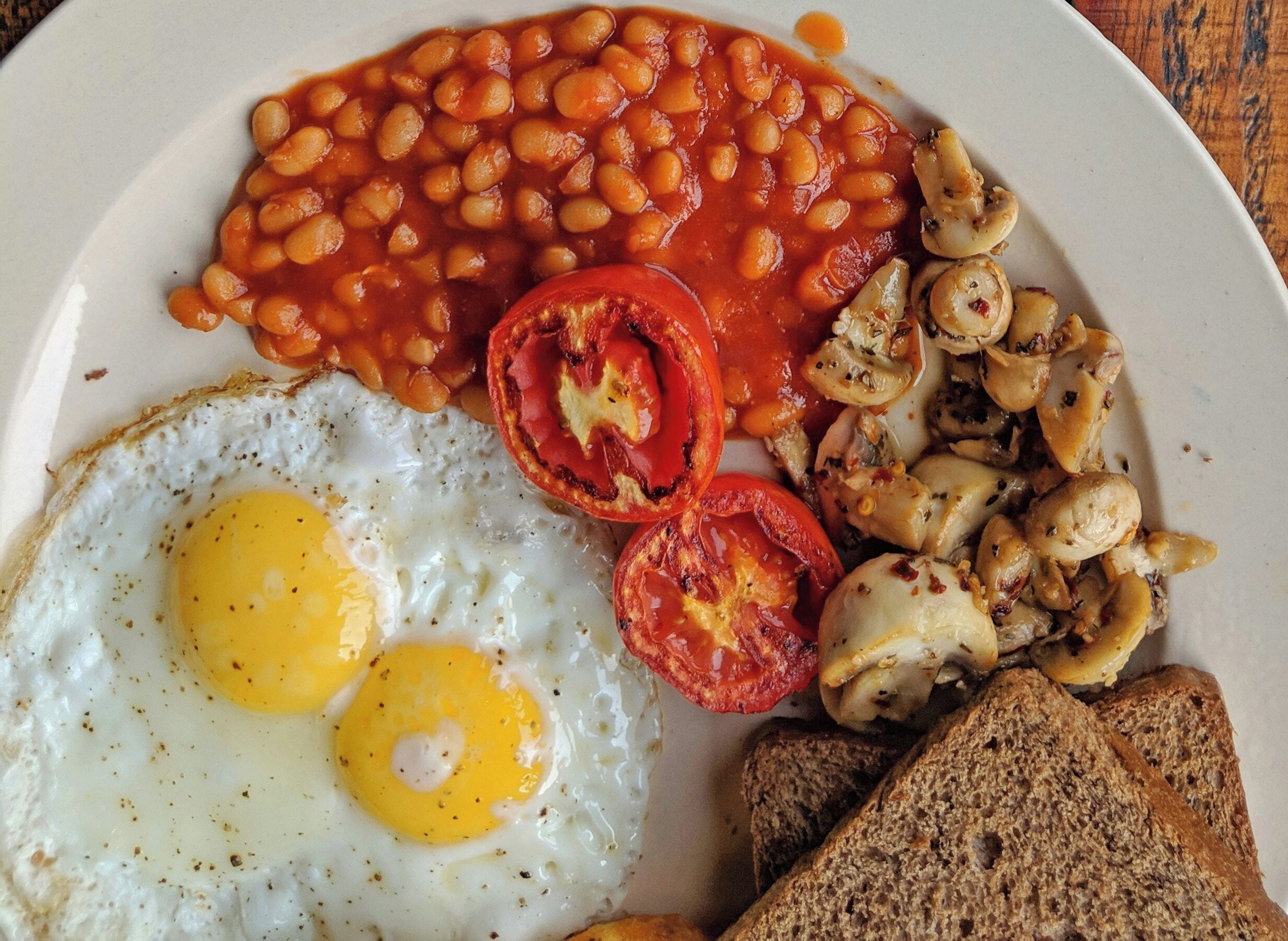 Un plato con huevos, frijoles, champiñones, tomates y tostadas.