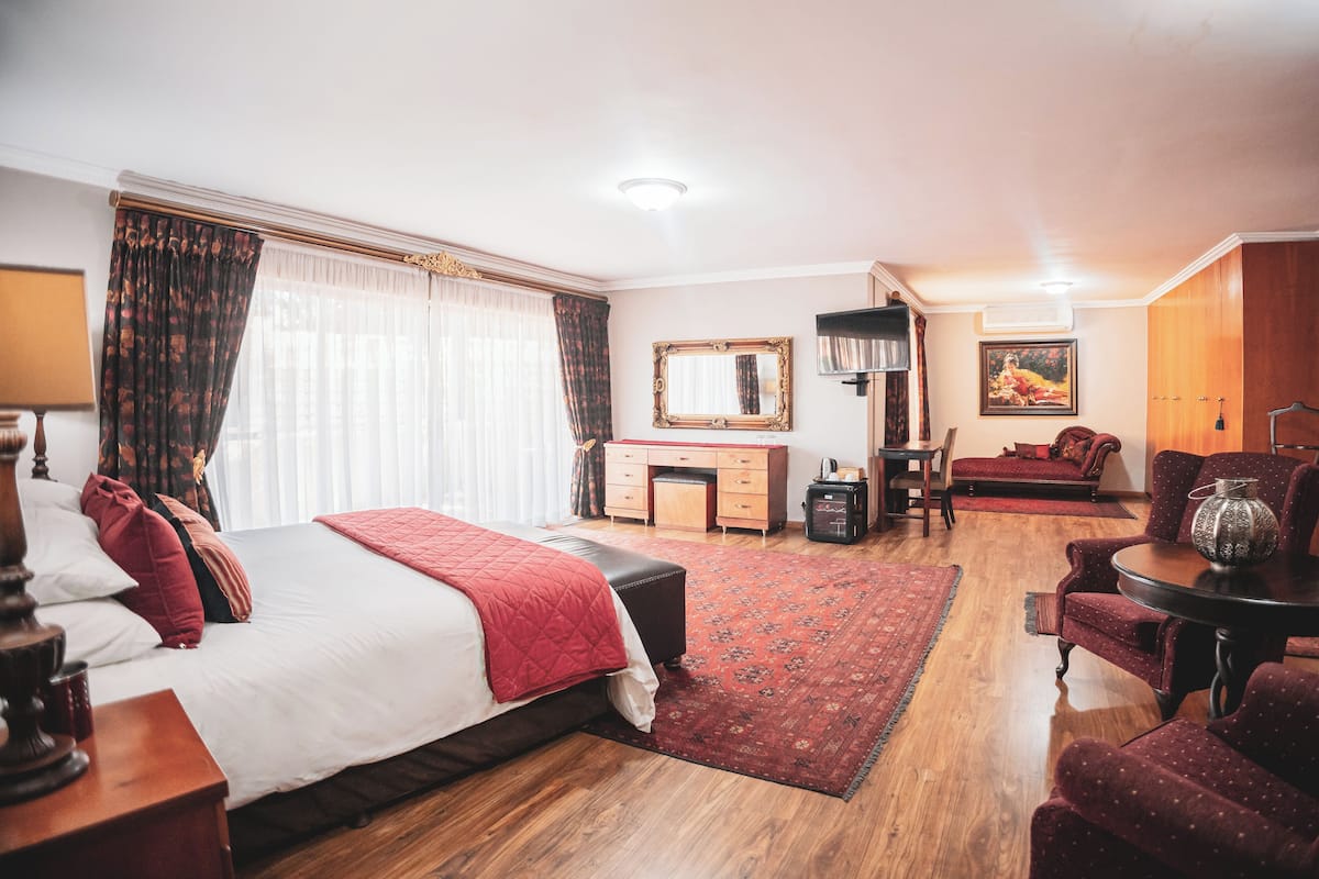 A hotel room with a large bed, a desk, a chair, a sofa, and a TV.