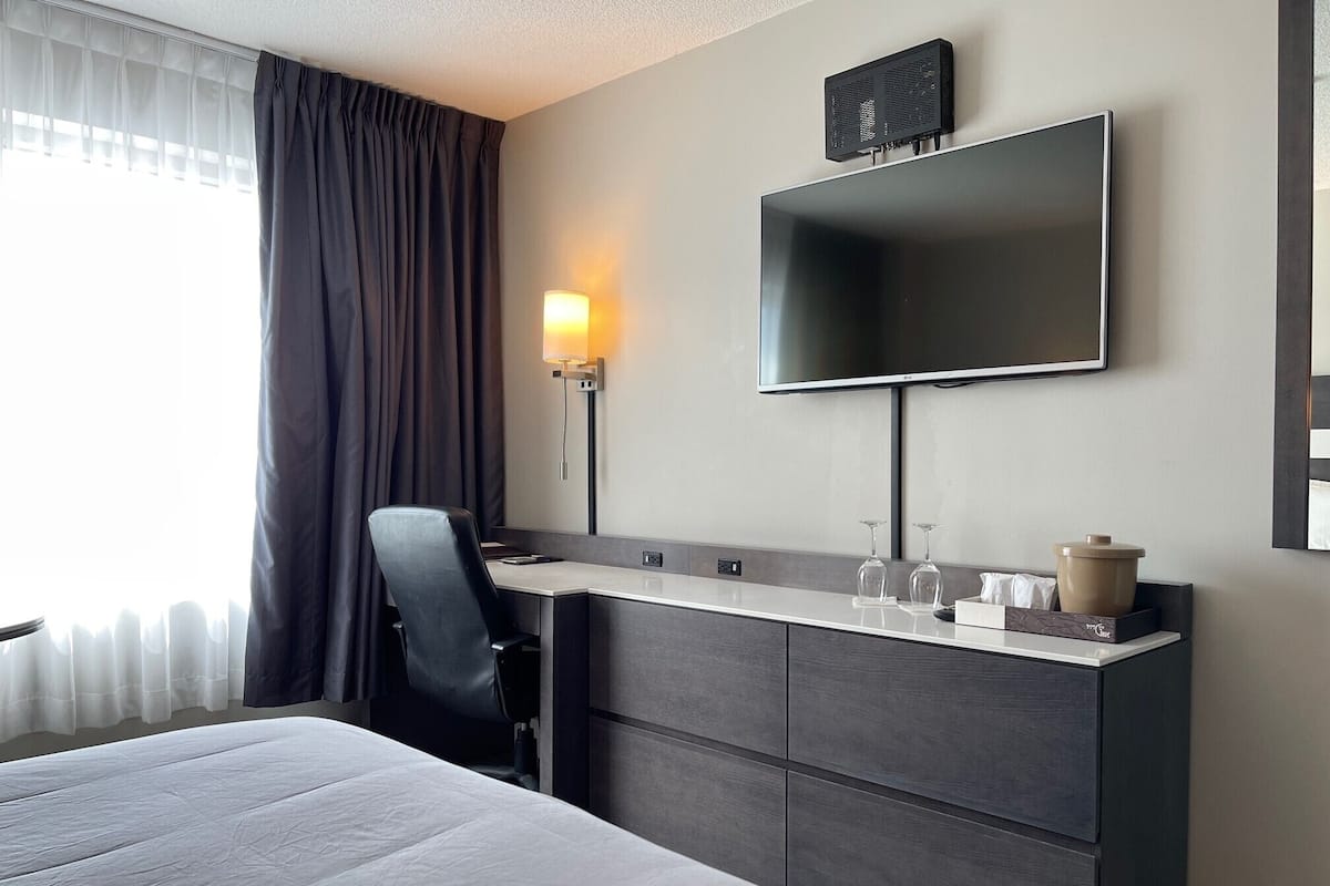 Una habitación de hotel moderna con una cama, un escritorio con silla, un televisor de pantalla plana y una lámpara.