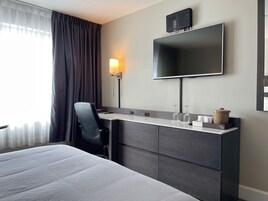 Una habitación de hotel moderna con una cama, un escritorio con silla, un televisor de pantalla plana y una lámpara.
