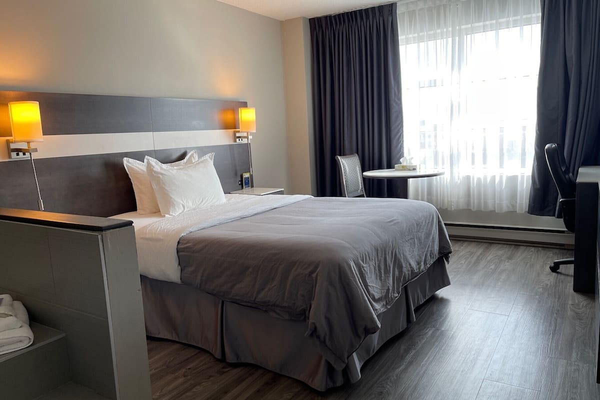 Una habitación de hotel con una cama grande, un escritorio, una silla y una pequeña mesa.