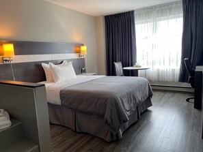 Hotellihuone, jossa on suuri sänky, työpöytä, tuoli ja pieni pöytä.