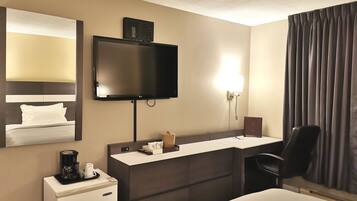 A hotel room with a bed, a desk, a TV, a coffee machine, and a trash bin.