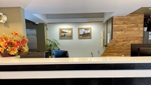 A reception area with a white reception desk, two framed pictures on the wall, a wooden accent wall, and a potted plant. - Auberge de la Gare (Gatineau)