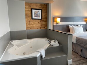 A modern bathroom with a freestanding bathtub, a wooden accent wall, and a bed with a headboard and bedside lamps. - Auberge de la Gare (Gatineau)