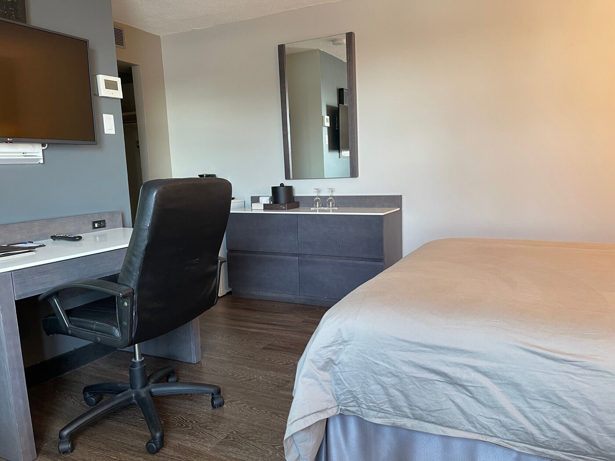 A hotel room with a bed, a desk with a chair, a dresser, a mirror, and a television.