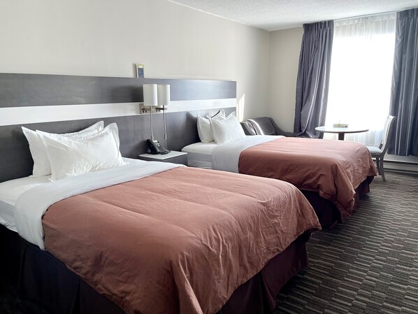 Hotellihuone, jossa on kaksi sänkyä, pieni pöytä, tuoli ja näkymä ulos.