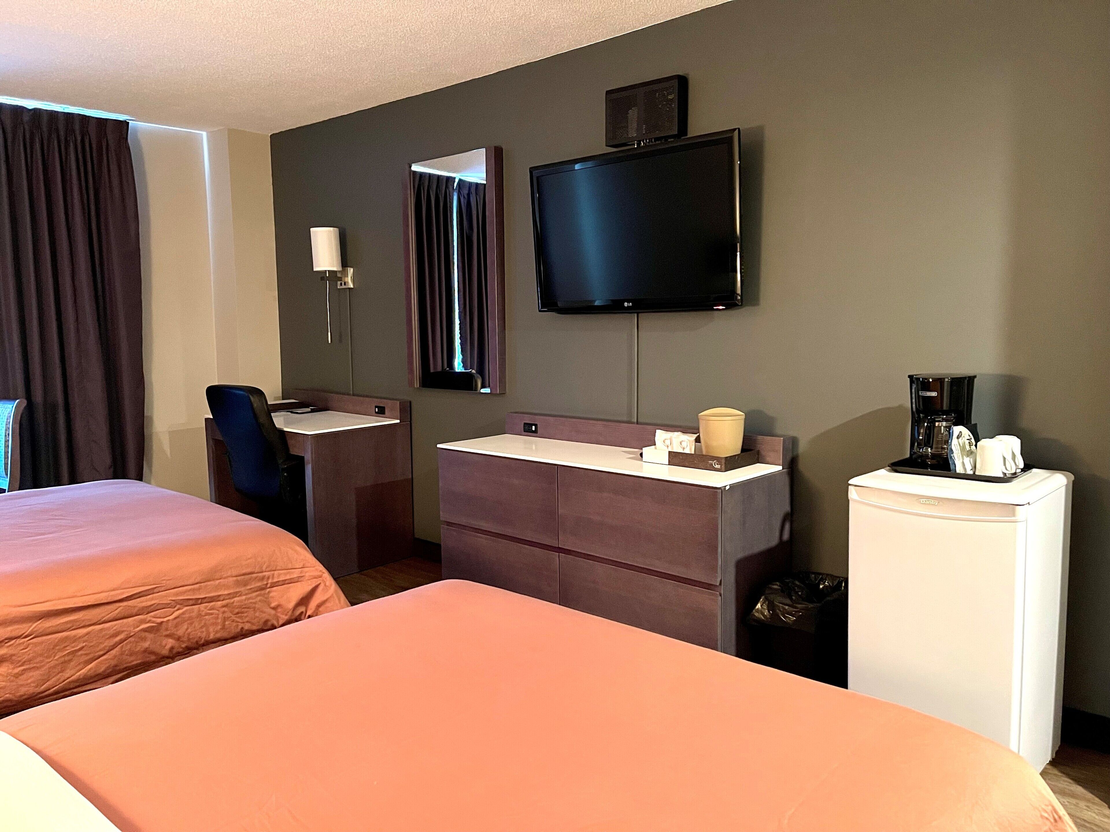 Habitación de hotel con dos camas, televisor, lavamanos y cafetera.