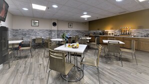 A spacious dining area with multiple tables and chairs, a kitchen area with a counter and appliances, and a decorative wall with a clock and framed pictures. - Auberge de la Gare (Gatineau)
